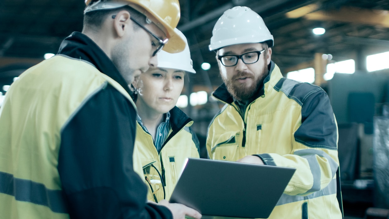 Two workers wearing helmets discuss a data.